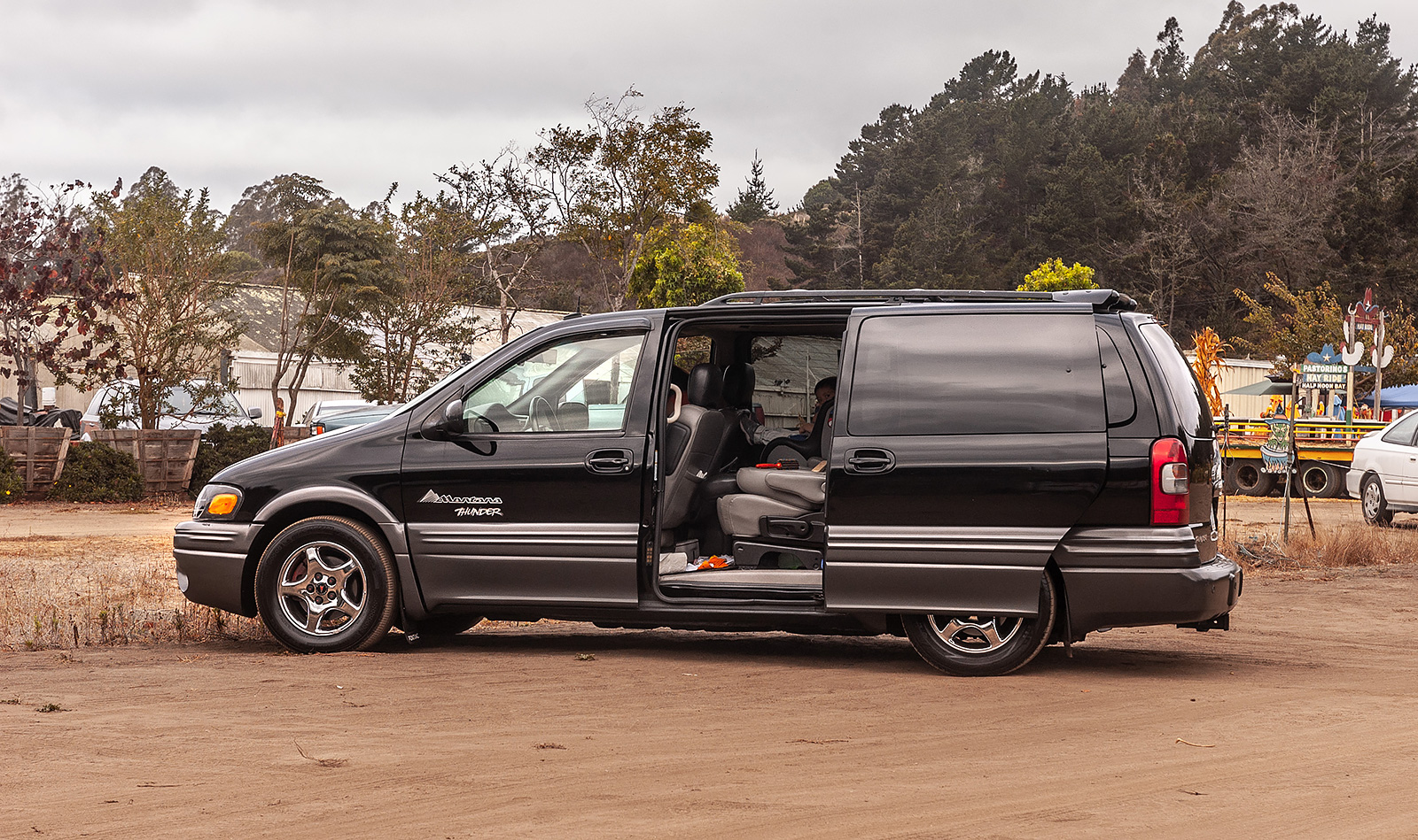 Side view of a 2003 AWD Pontiac Montana Thunder in black, with an open sliding side door, parked near Lemos Farm, Half Moon Bay, California during Halloween